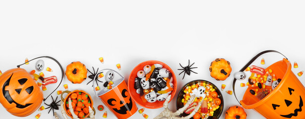 Halloween trick or treat bottom border with jack o lantern pails and a variety of candy. Top view on a white banner background with copy space.