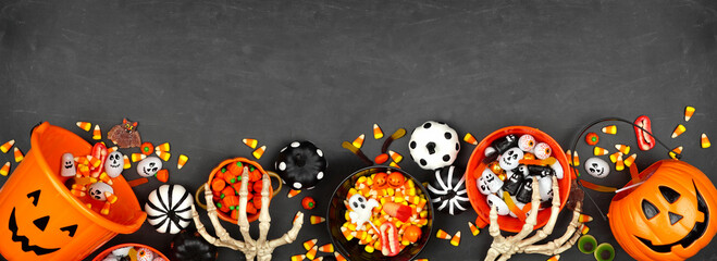 Halloween trick or treat bottom border with jack o lantern pails and mixed candy. Top view on a black banner background with copy space.