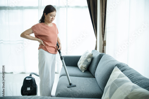 Asian housewife using a wireless vacuum machine to clean a sofa in living room close up. 