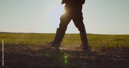 Farmer walks in rubber boots down a farmer field dust rising from shoes. Low angle. One part is sown, the second part is not sown.