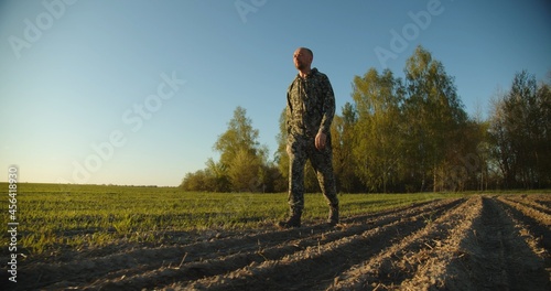 Farmer walks through a young green field during sunset. Adult man farmer walking and checks his agriculture field. Worker walking on agriculture field.