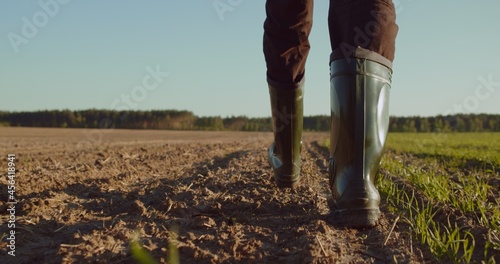 Low angle: man walking in rubber boots in a farmer's field, the blue sky above the horizon. Man walking through an agricultural field. Farmer walks through a plowed field in early spring. photo
