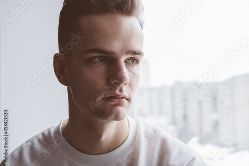 Young sad pensive guy, teenager sits and looks out the window