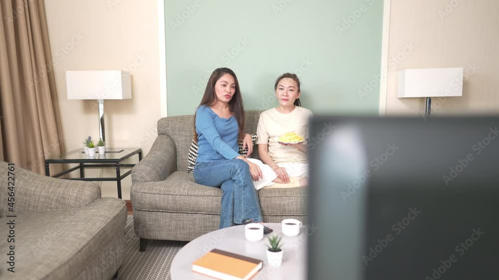 4K Millennial Asian woman friends sitting on sofa watching movie on tv with eat snack together in living room. Female friendship enjoy and having fun weekend activity lifestyle with home entertainment 4K Millennial Asian woman friends sitting on sofa watching movie on tv with eat snack together in living room. Female friendship enjoy and having fun weekend activity lifestyle with home entertainment