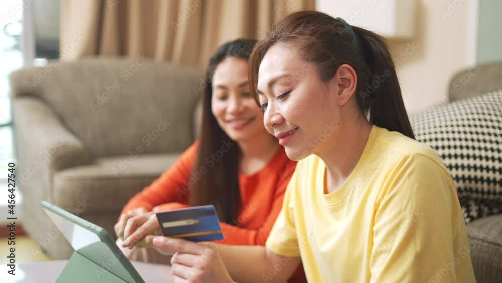 4K Asian woman friends sitting in living room using digital tablet for online shopping with credit card together. Modern female friendship enjoy weekend activity lifestyle with technology at home. 4K Asian woman friends sitting in living room using digital tablet for online shopping with credit card together. Modern female friendship enjoy weekend activity lifestyle with technology at home.