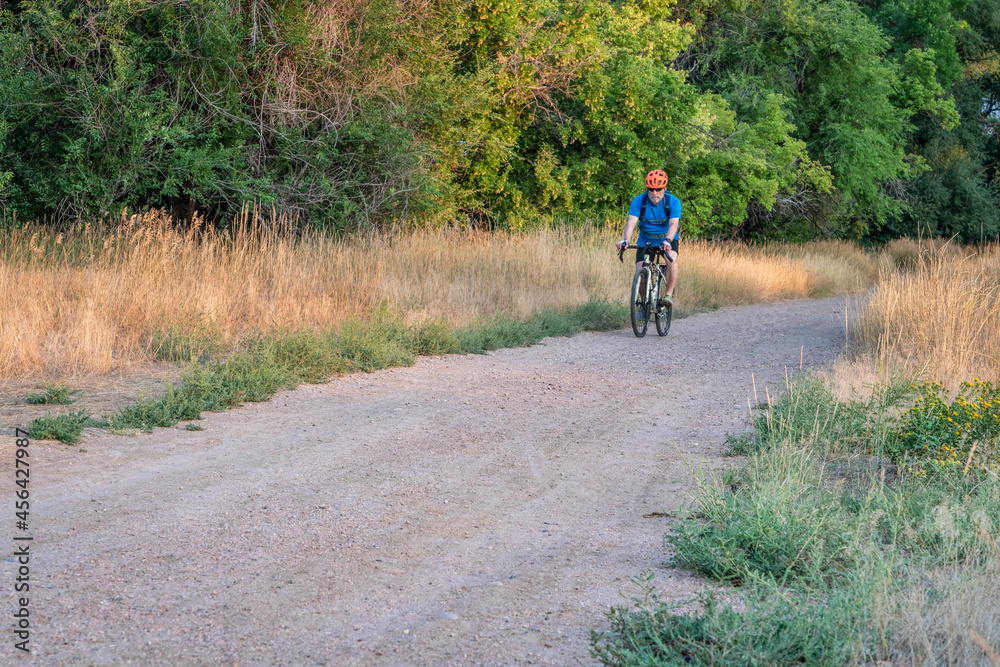 senior male cyclist is riding a touring bike on a gravel trail along the Poudre River in Fort Collins, Colorado, late summer scenery