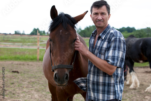A man stands with a horse on a ranch on a sunny day, looks at the photographer and is happy..