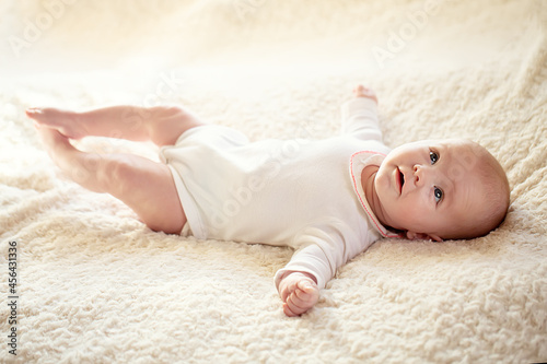 A charming baby in a white sunny bedroom. A newborn baby is resting in bed. Children's room for small children. Textiles and bed linen for children. Family morning at home. 