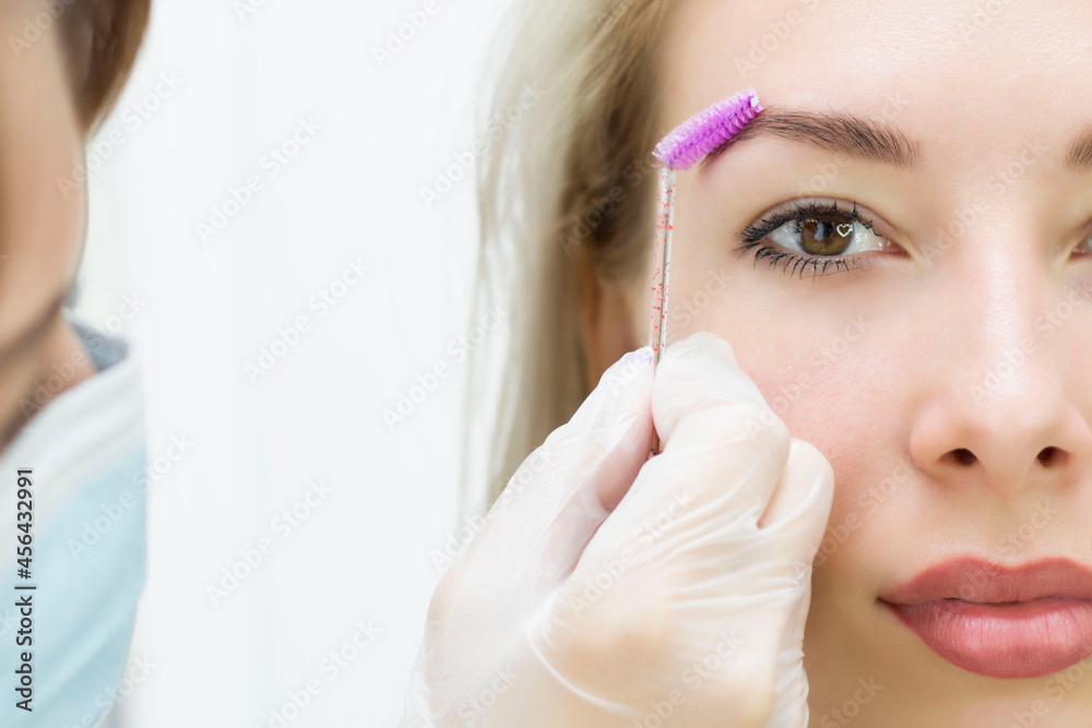 A young woman combs her eyebrows with a pink brush. Eyebrow correction, henna staining. Close-up. Half of the face. A young woman combs her eyebrows with a pink brush. Eyebrow correction, henna staining. Close-up. Half of the face.