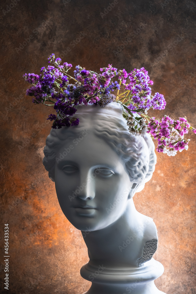 Plaster bust of the beautiful Aphrodite with flowers on her head on a rusty antique background.