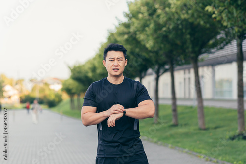 Male asian athlete, tired after a morning jog, runs in the park near the stadium