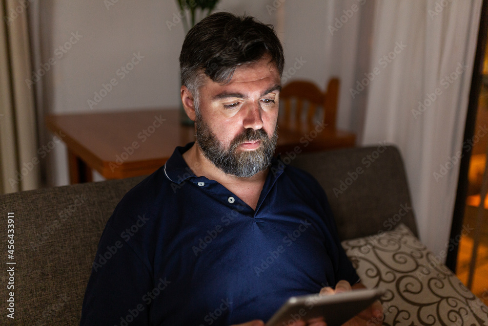 bearded man on sofa uses digital tablet in dining room overnight bearded man on sofa uses digital tablet in dining room overnight