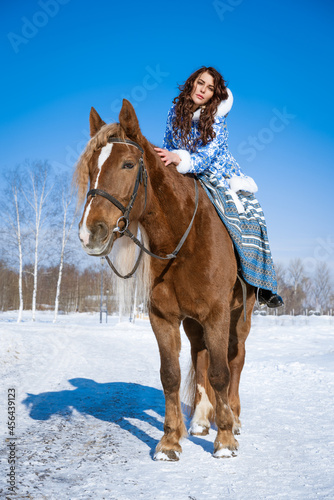 beautiful young, dark-haired woman, in traditional clothes, riding a horse in winter