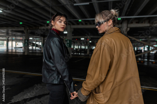 two beautiful young fashion girls with cool leather jacket walking in a parking lot in the city