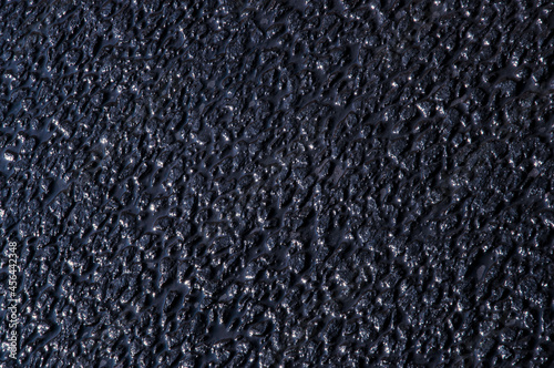 Texture of a wet asphalt road with cracks close-up of a dark blue shade