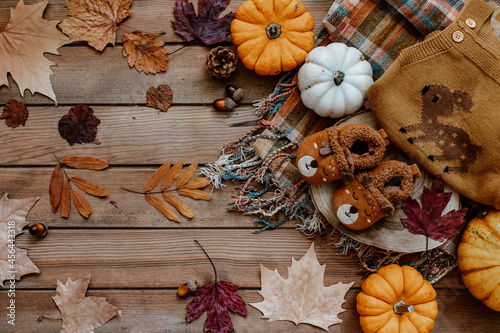 Baby autumn wear clothes with pumpkins and leaves on brown background. Top view. Cute warm kid autumn bodysuit and booties. Autumn baby shower