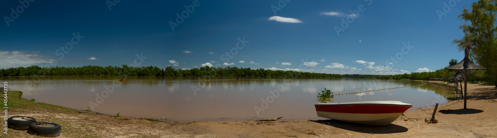 Panorama view of the river shore in a summer sunny day. A boat in the sand in the foreground and the tropical jungle in the background reflected in the water.  