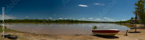 Panorama view of the river shore in a summer sunny day. A boat in the sand in the foreground and the tropical jungle in the background reflected in the water. 