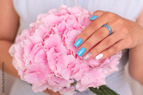  Beautiful female hand with blue manicure nails holding hydrangea flower 