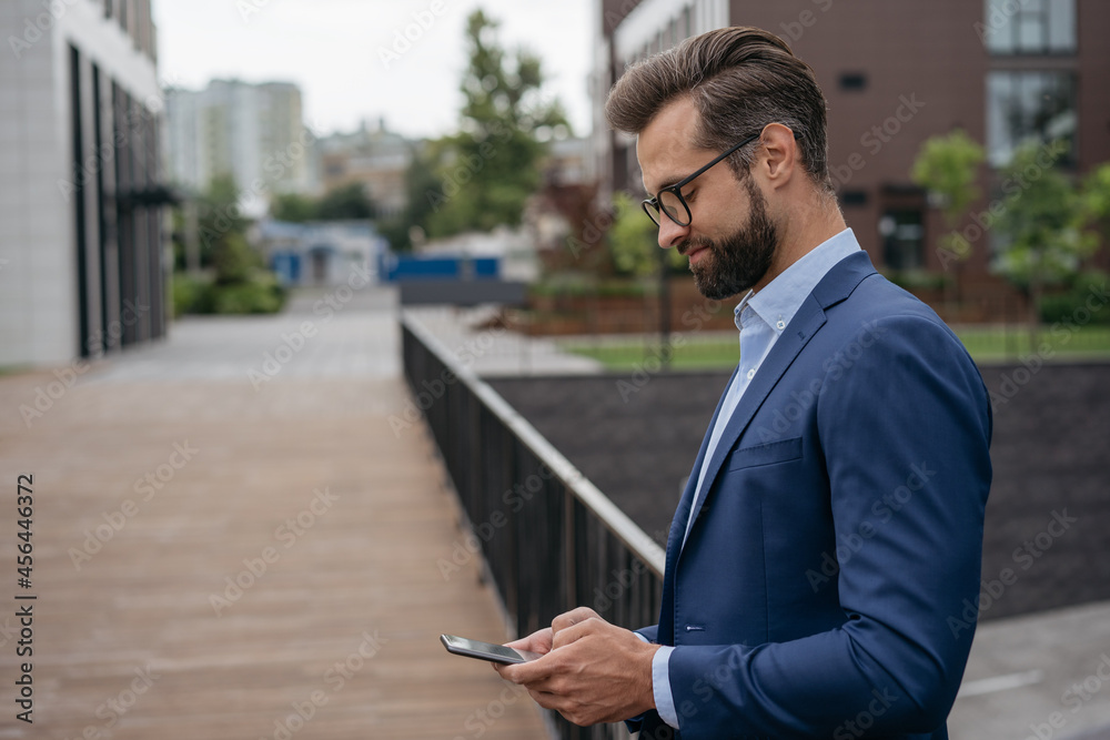 Confident businessman working, communication online standing on the street, copy space. Handsome bearded man holding mobile phone, ordering food using modern technology Confident businessman working, communication online standing on the street, copy space. Handsome bearded man holding mobile phone, ordering food using modern technology