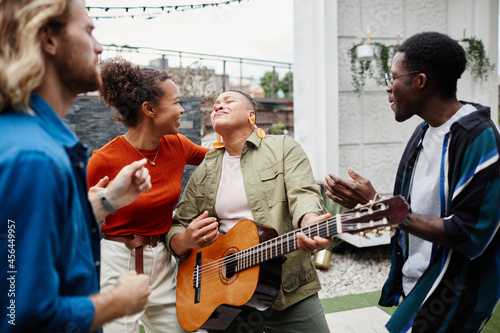 Diverse group of young people playing guitar and having fun while enjoying outdoor party at rooftop
