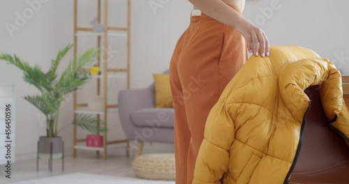 Young woman hanging puffer jacket on the back of chair at home