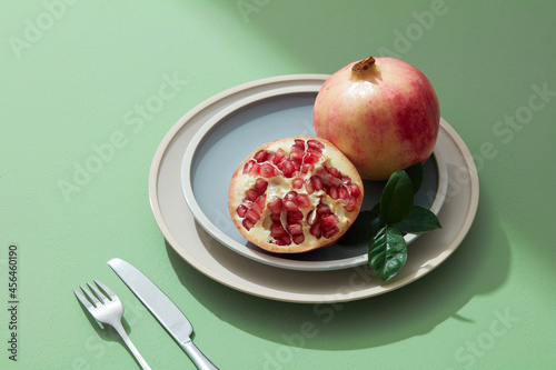 Still life of red pomegranate fruit, seed, half on pastel plate with light green background. 