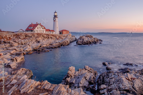 Moments before the sun rises a soft pink light is cast across the Portland Head Lighthouse and the rocks