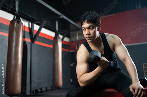 Handsome adult Asian men sweating while lift up the dumbbell workout for arm biceps muscle part inside of fitness gym. Bodybuilding athlete sport training for body strength and good health.
