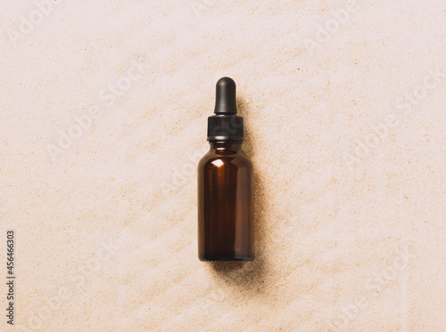 Bottle of serum oil cosmetic product beach sand background. Abstract podium product presentation on a sandy background