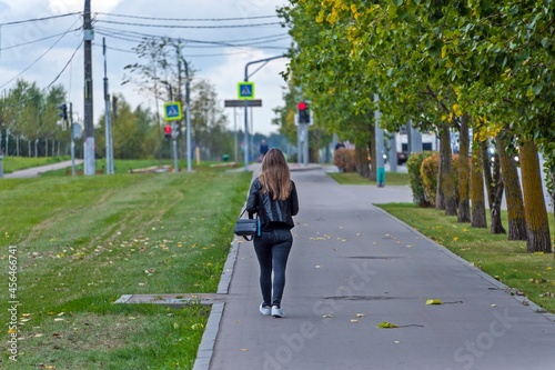 A girl with loose hair walks along the alley of the park