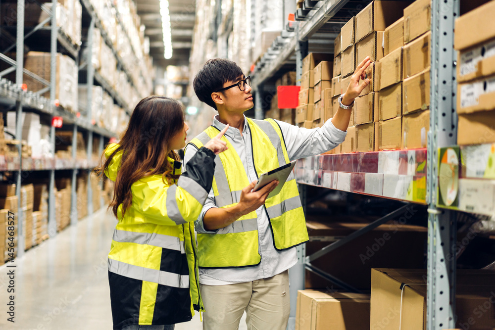 Asian two engineer in helmet team order detail on tablet computer for checking goods and supplies on shelves with goods background in warehouse.logistic and business export Asian two engineer in helmet team order detail on tablet computer for checking goods and supplies on shelves with goods background in warehouse.logistic and business export