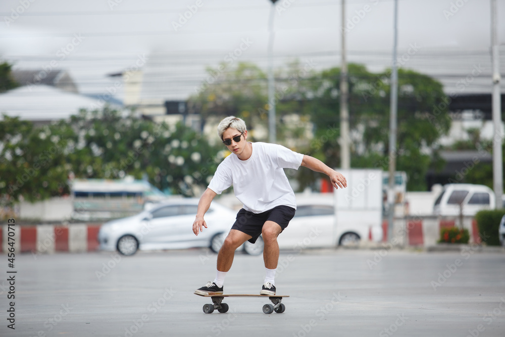 asian young man wear sunglasses playing skateboard on street city.  skateboarding outdoor sports. extreme sports concept.