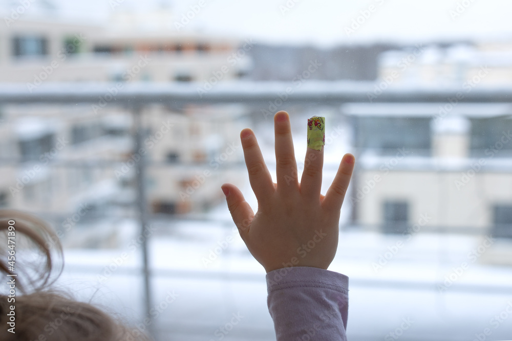 Sad child patients in hospital clinic stand at window to look out, put her hand palm and finger bandaged playful Band-aid plaster on window.want to go home.waiting parents family mother
