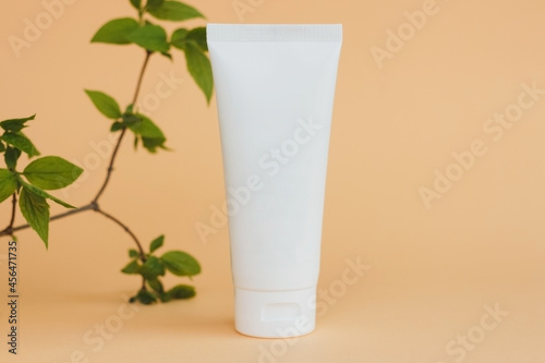 cosmetic cream tube with green leaves on beige background. Eco natural cosmetics concept