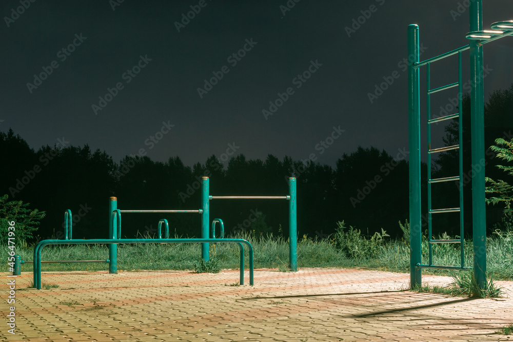 Empty sports ground with exercise equipment at night in a park illuminated by a lantern Empty sports ground with exercise equipment at night in a park illuminated by a lantern