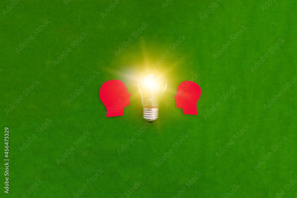 Two silhouettes of a red man's head look at an electric light bulb on a green background. The concept of joint ideas.