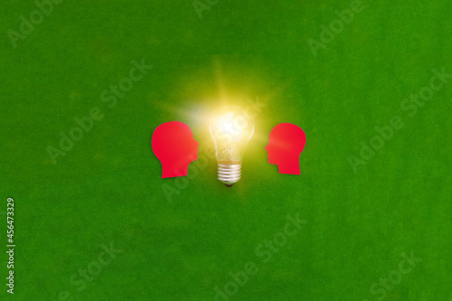Obraz na płótnie Two silhouettes of a red man's head look at an electric light bulb on a green background. The concept of joint ideas. w salonie