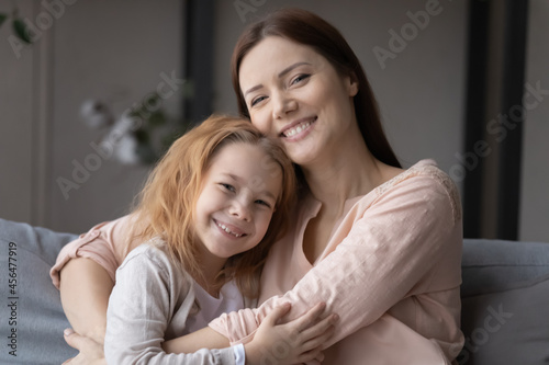 Portrait of affectionate young woman cuddling smiling little preschool child daughter, showing tender feelings at home. Joyful two different generations family enjoying loving moment together indoors.