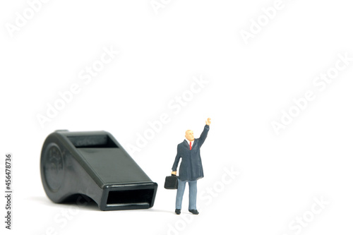 Miniature people toy figure photography. Whistle blower concepts. A businessman standing in front of black whistle while raise his hand. Isolated on white background