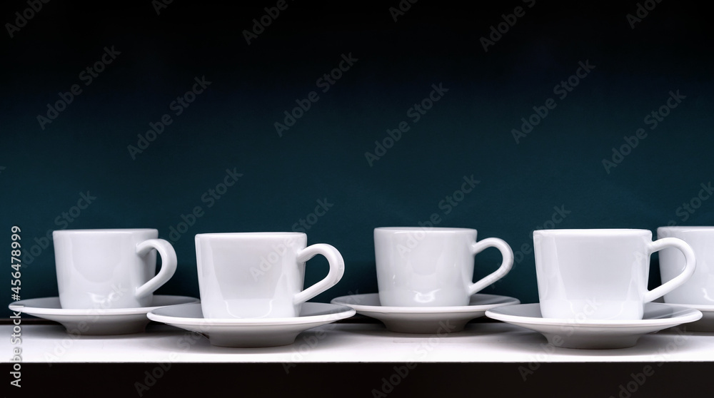 White coffee cups with saucers on a dark green background.
