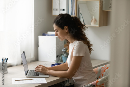 Focused 35s woman journalist freelancer sit at desk work online on laptop. Businesswoman e-mailing to client  make assignment studying use internet  modern tech business professional app usage concept