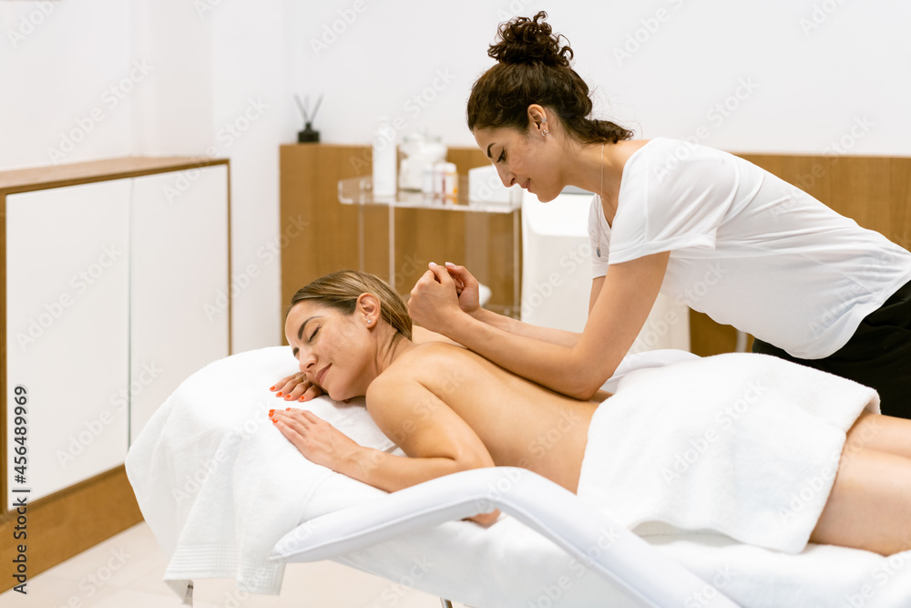 Female masseuse giving a back massage to a woman in a beauty parlour.