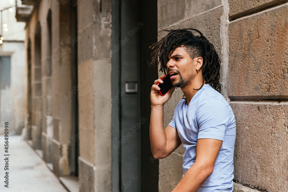 horizontal portrait of a latin american man with dreadlocks talking by phone. He is in the street and looks angry