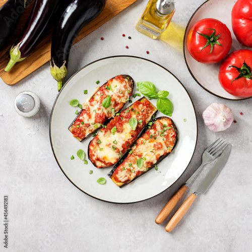 Baked eggplant with mozzarella cheese, chopped tomatoes and fresh basil leaves. Vegetarian food recipe. Light gray background, top view. 