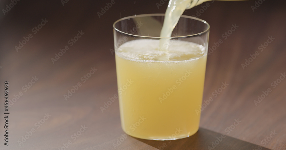 pour orange juice from glass bottle into tumbler glass on walnut table pour orange juice from glass bottle into tumbler glass on walnut table