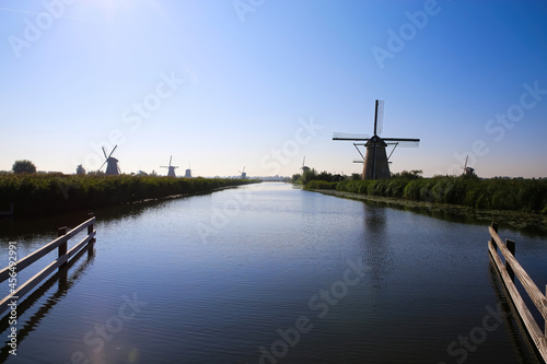View over dutch water canal on horizon with windmills in rural landscape in morning sun light and dizzy blue sky - Kinderdijk, Netherlands
