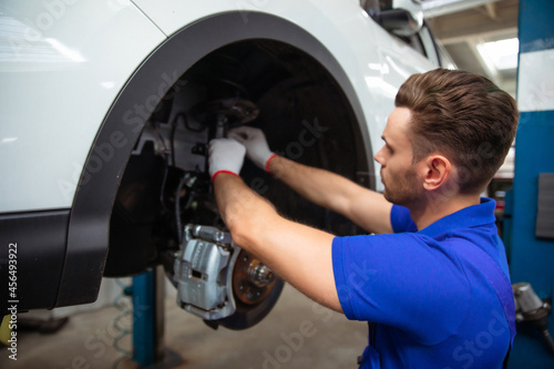 Young auto mechanic in a special suit repairs the brake system of a car or changes the brake pads
