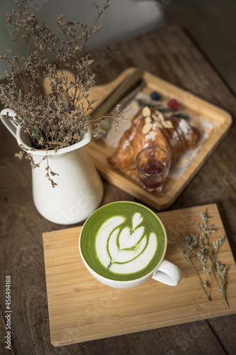 Cup of green tea matcha latte foam art with fresh croissants and ripe berries and jam background on wooden table.