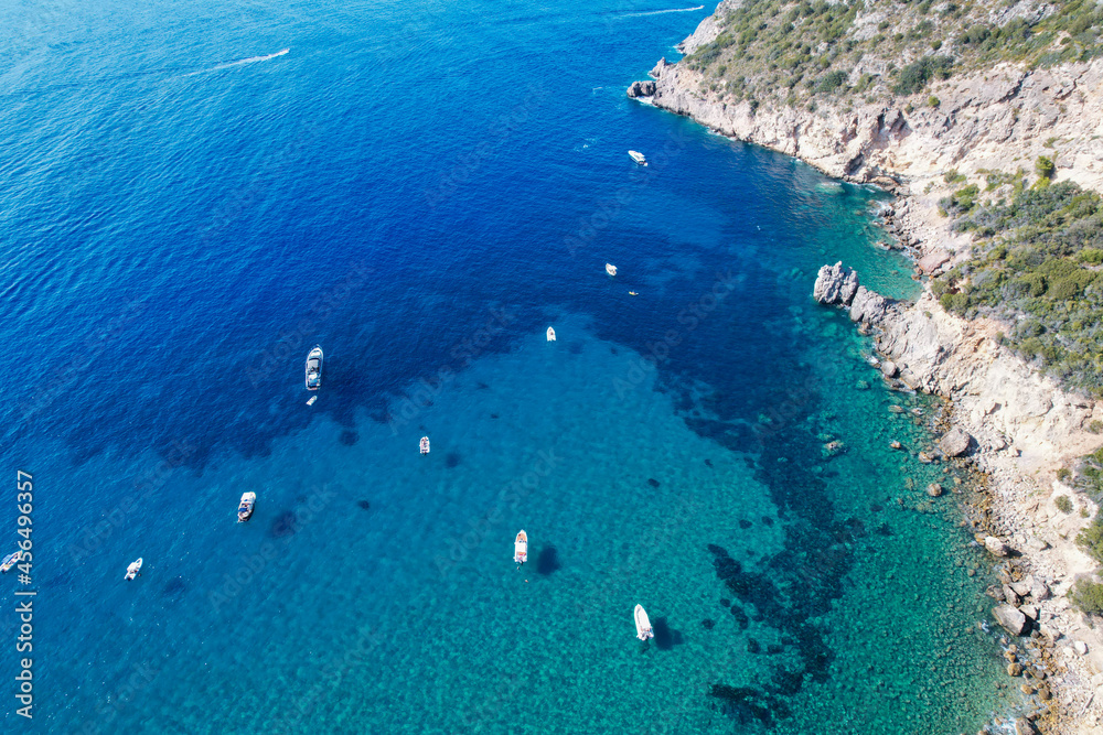 View from above, stunning aerial view of a bay with boats and luxury yachts sailing on a turquoise, clear water surrounded by cliffs. Porto Santo Stefano, Monte Argentario, Italy.